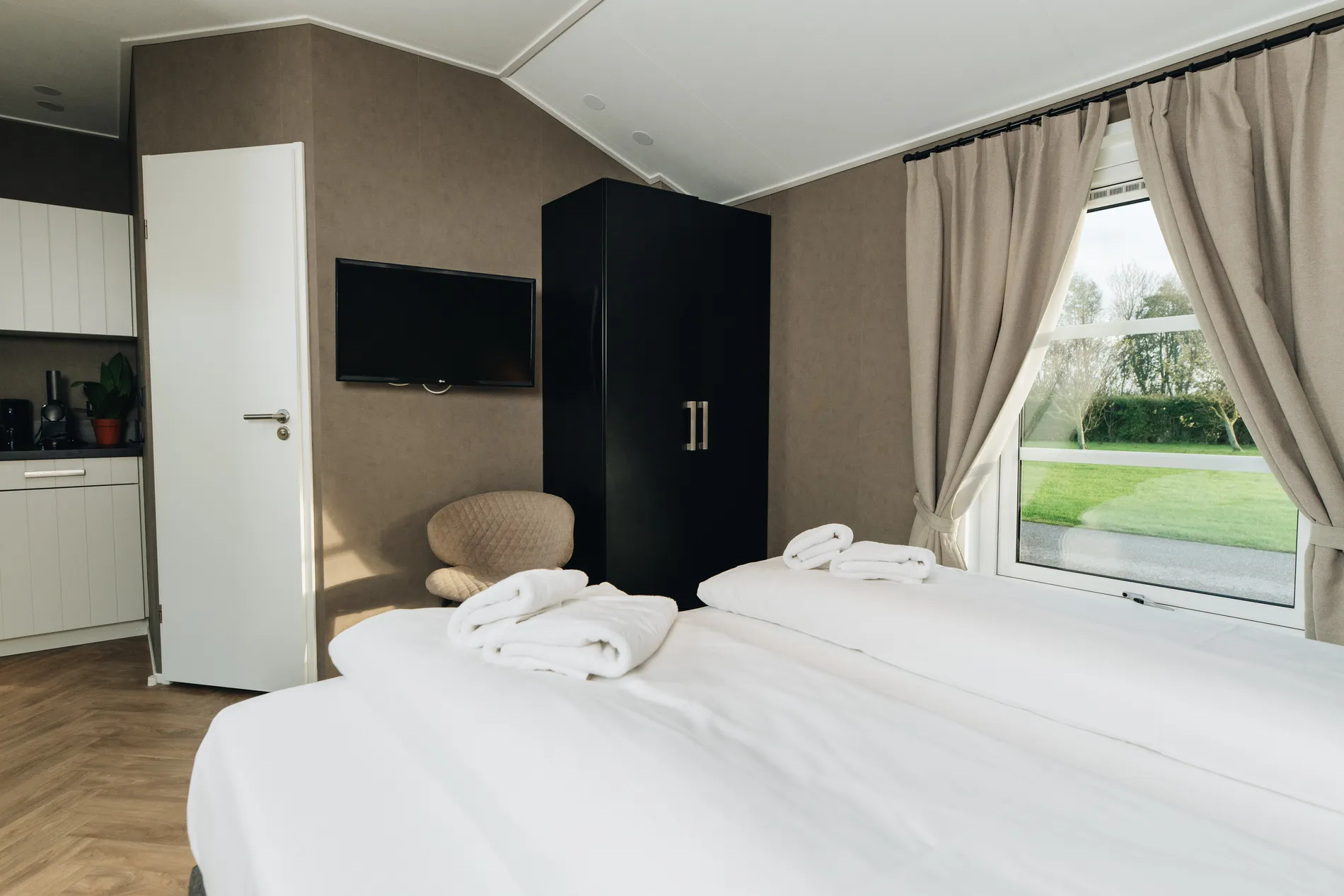 Modern slaapkamerinterieur van een lodge met een zwarte kledingkast, aan de muur gemonteerde tv en grote ramen die zorgen voor veel natuurlijk daglicht.